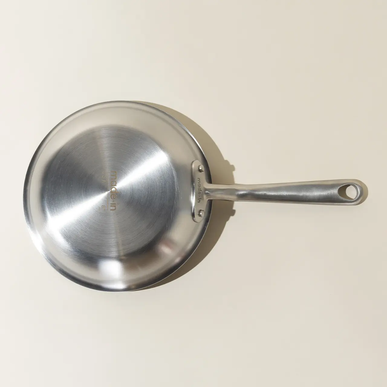 A stainless steel frying pan is shown against a neutral background from a top-down perspective.