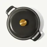 A black non-stick pan with a gold-colored center and two handles is displayed against a light background.