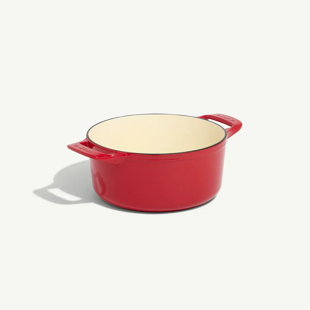 A red enameled cast iron Dutch oven sits on a light surface.