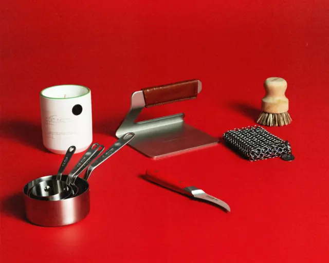 A collection of kitchen tools, including measuring cups, a bench scraper, a candle, and a brush, arranged on a vibrant red background.