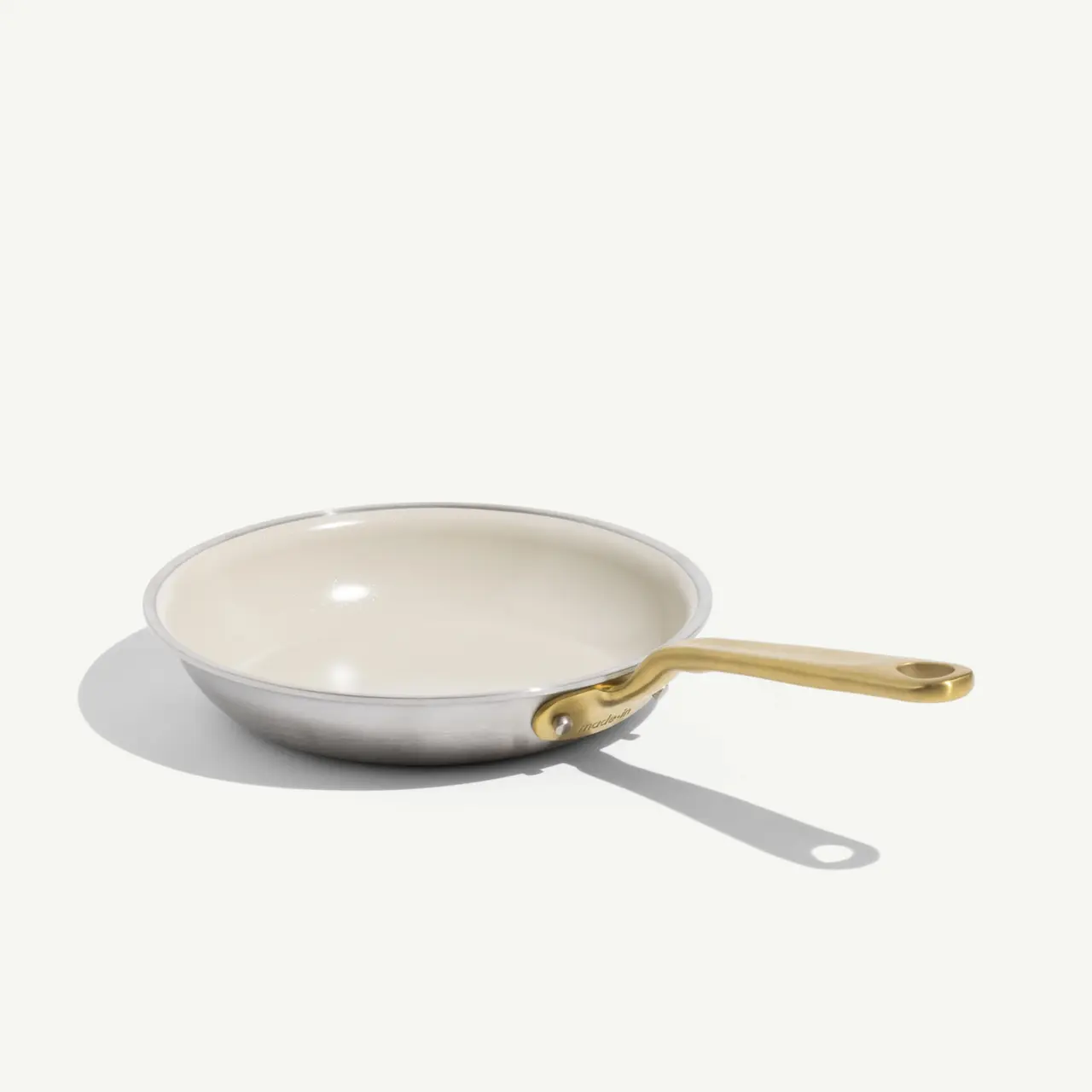 A shallow frying pan with a gold handle and a smooth, light-colored interior.