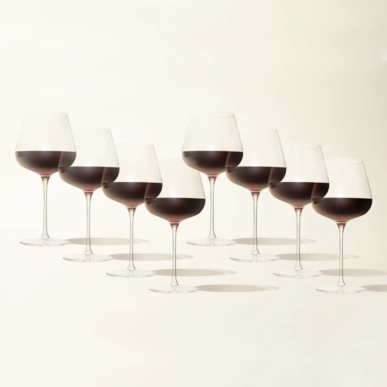 Seven wine glasses filled with red wine are arranged in a row against a light background.