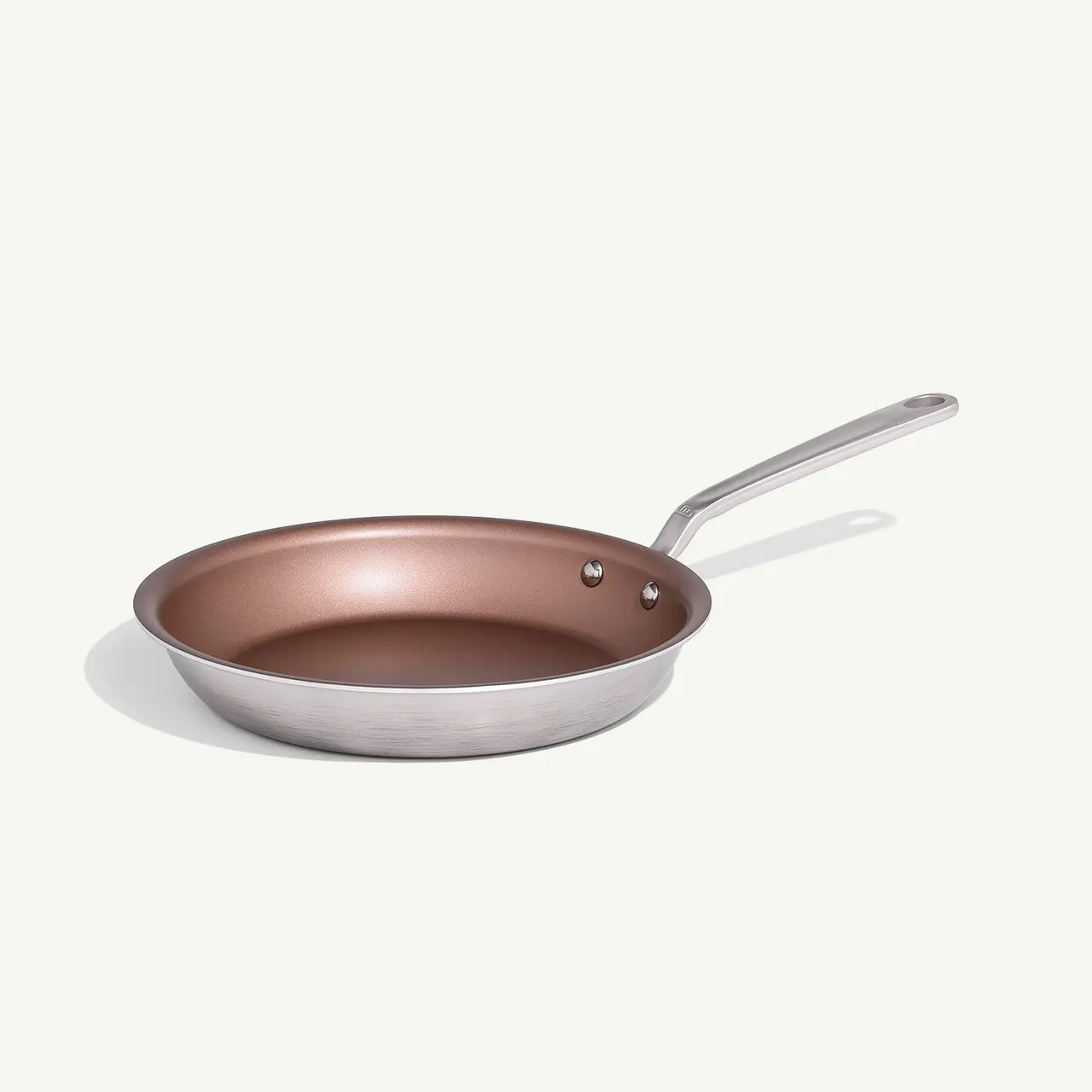 A stainless steel frying pan with a copper-colored interior sits against a plain background.