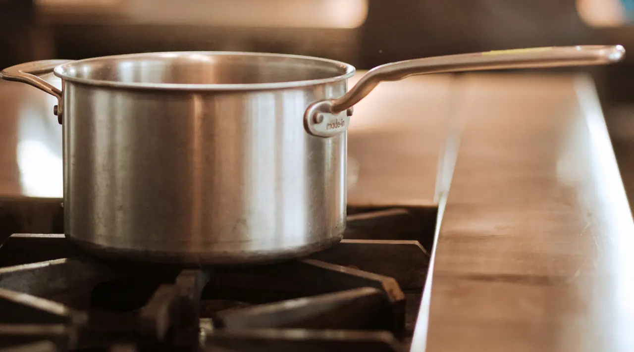 A stainless steel pot sits on a stove burner with a warm, blurred background.