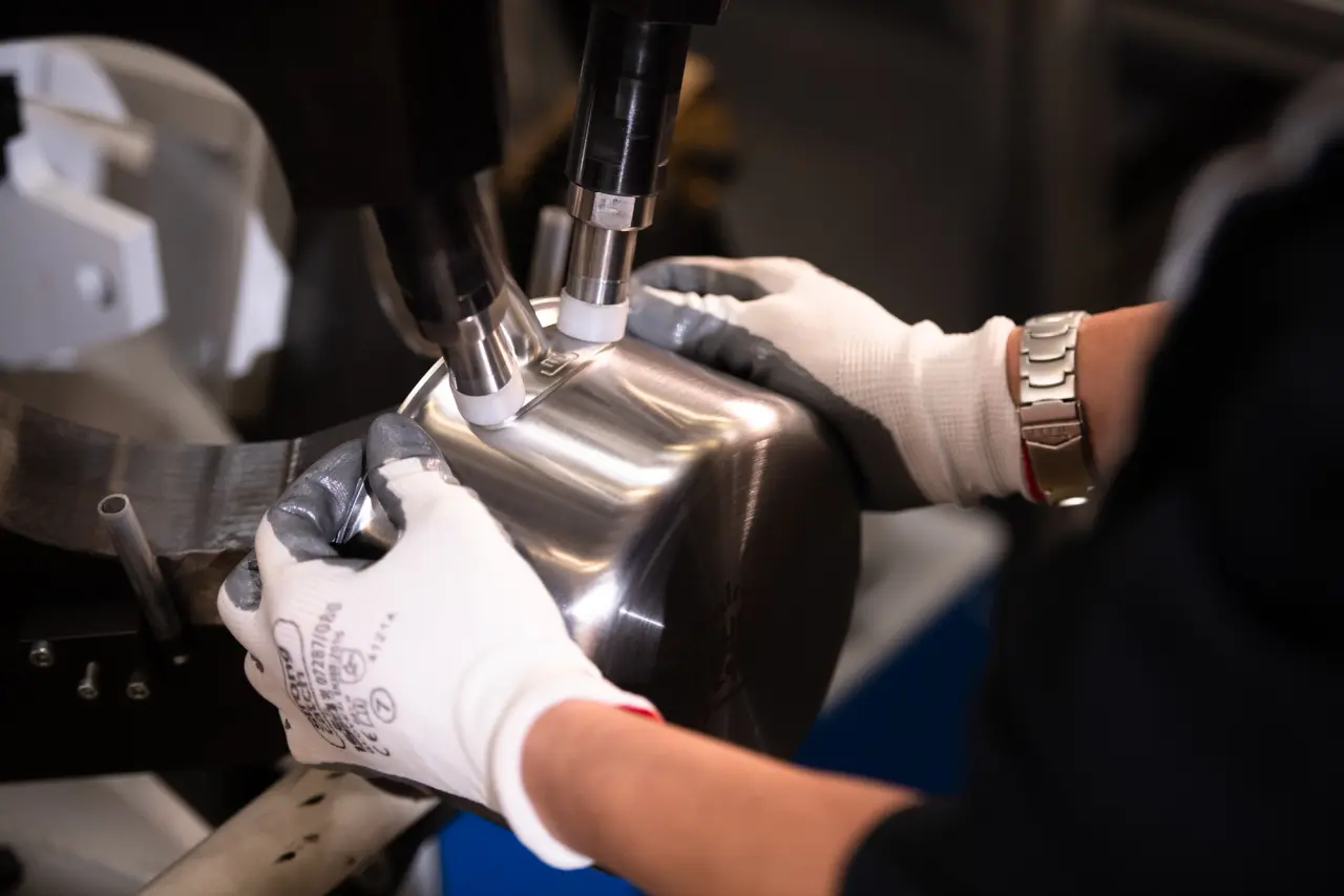 A person wearing gloves operates machinery to polish or work on a metal part.