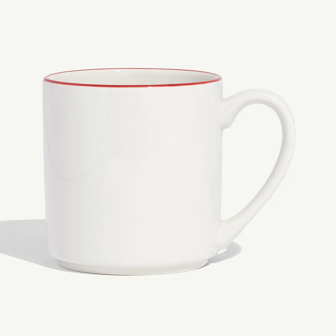 A white mug with a red rim on a light background.