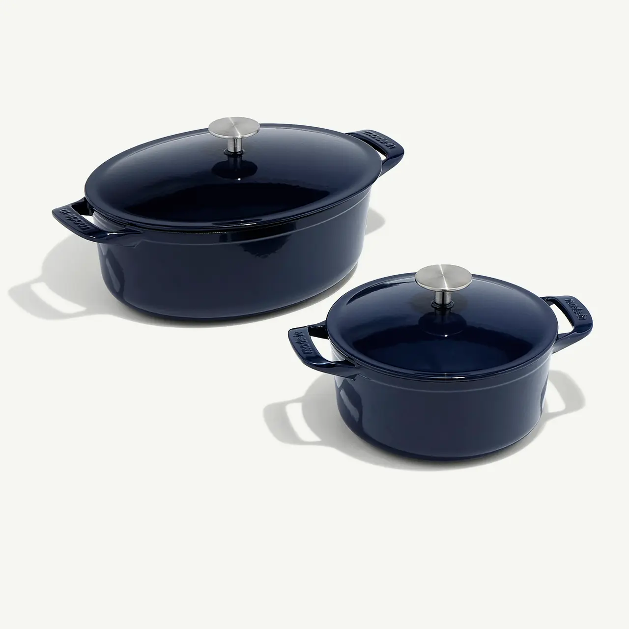 Two blue enameled cast iron pots with lids on a light background.