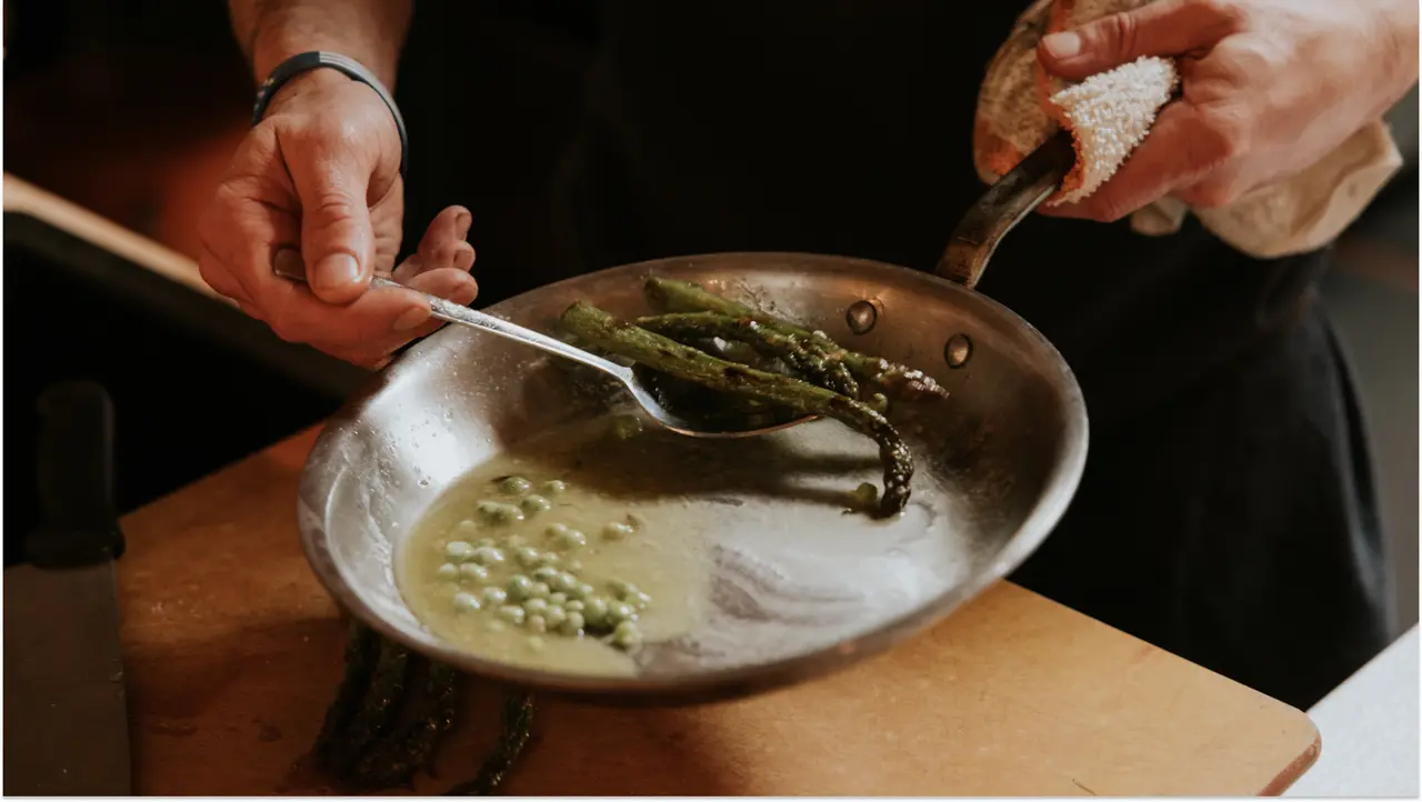 A person is sautéing asparagus in a pan over a stovetop, carefully lifting them with tongs.