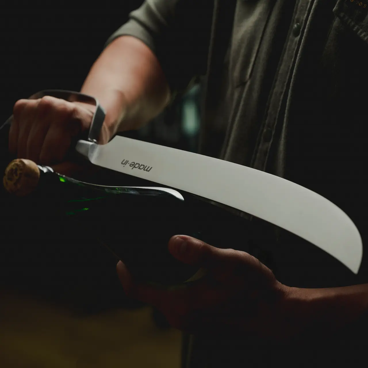 A person is elegantly opening a bottle of champagne with a saber, capturing the moment the bottle neck is severed.