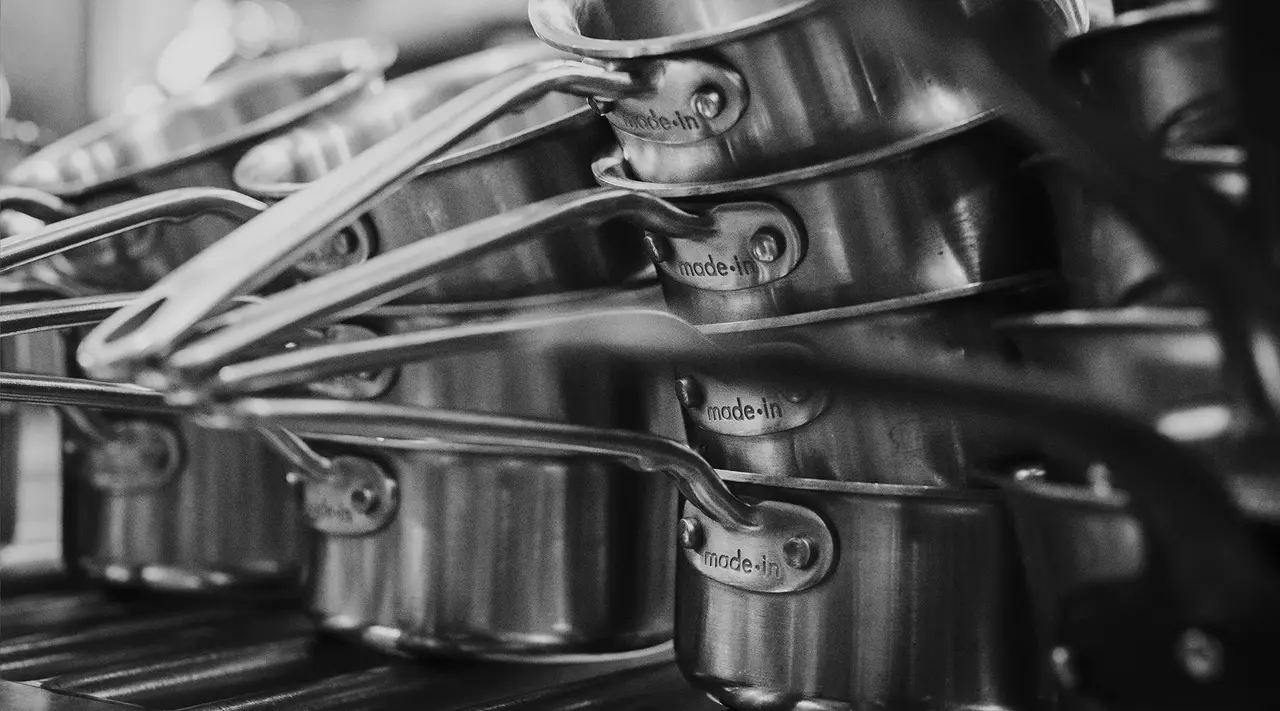 A stack of stainless steel pans with their handles aligned is neatly organized on a shelf, creating a pattern of repeating shapes.