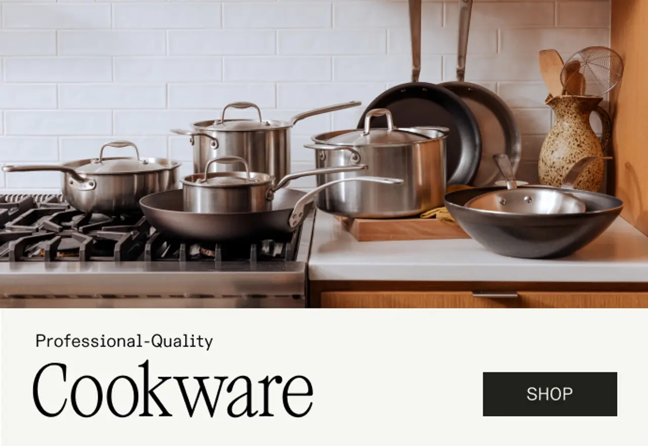 A modern kitchen countertop features an assortment of professional-quality stainless steel cookware, including pots and pans, alongside a decorative bowl.