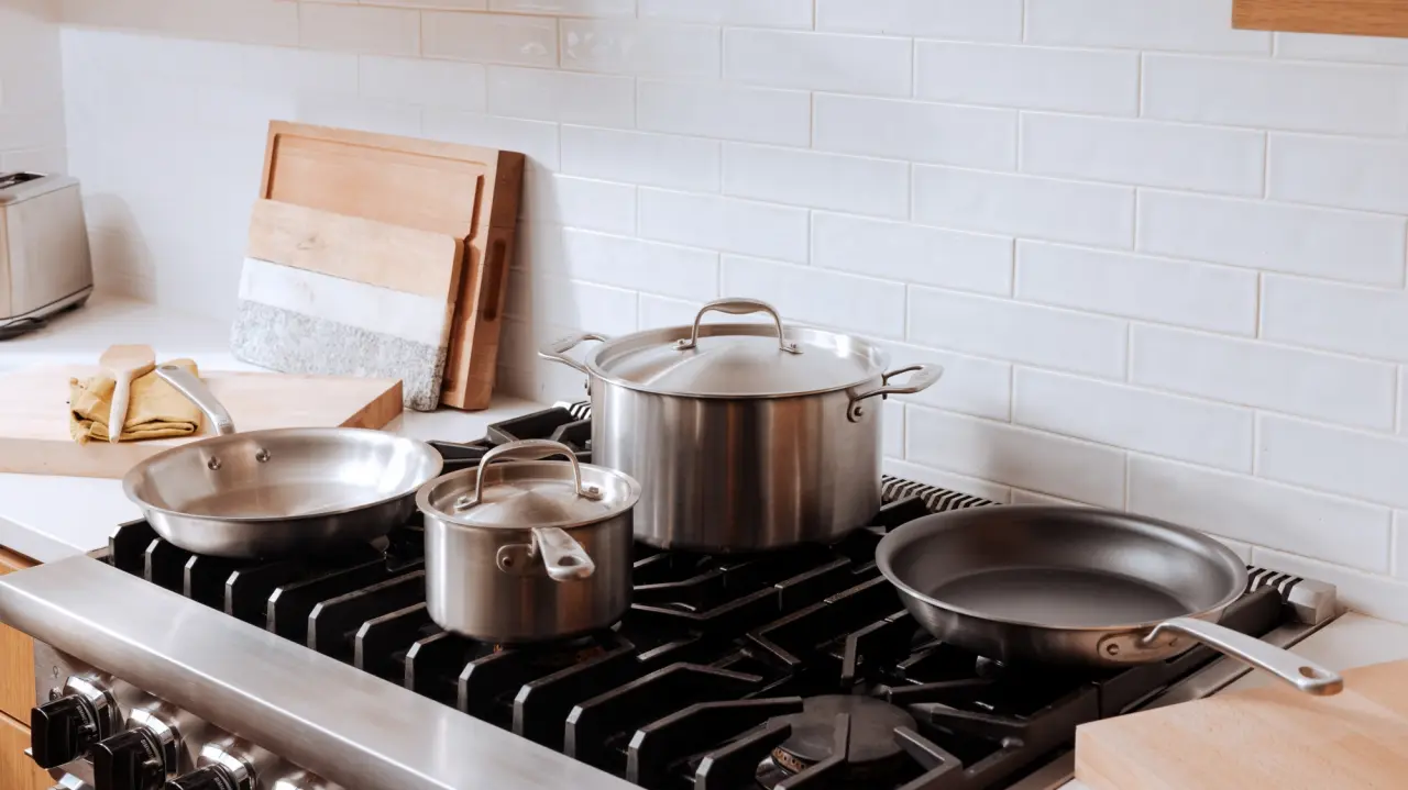 A modern kitchen stove top with various sizes of shiny pots and pans.