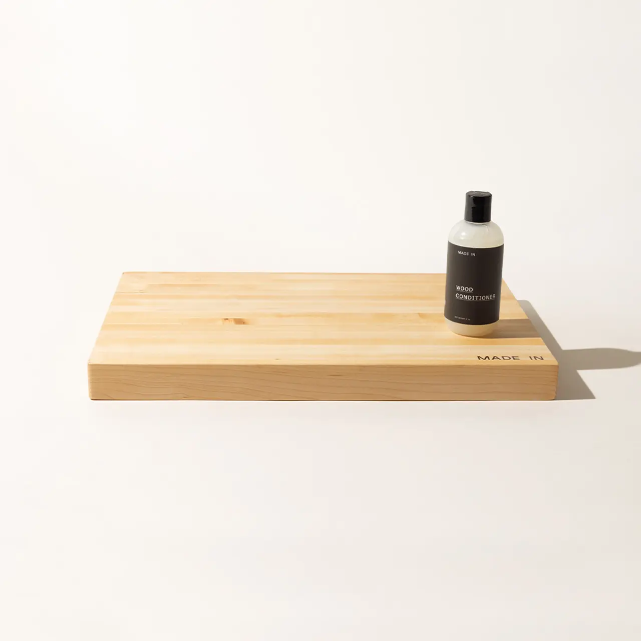 A wooden board with a dark-colored bottle labeled "Aesop" rests on a neutral background.