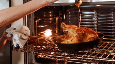 A person is basting a golden-brown roasted chicken in an oven.
