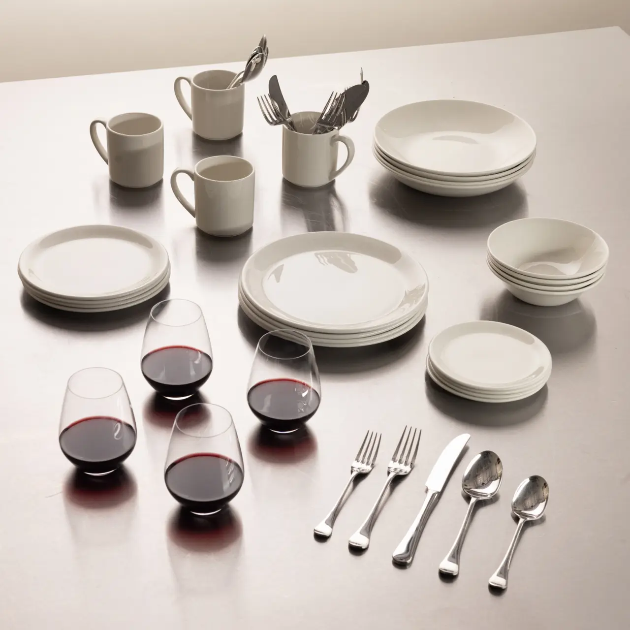 A neatly arranged dinnerware set including plates, bowls, cups, wine glasses, and cutlery on a table.