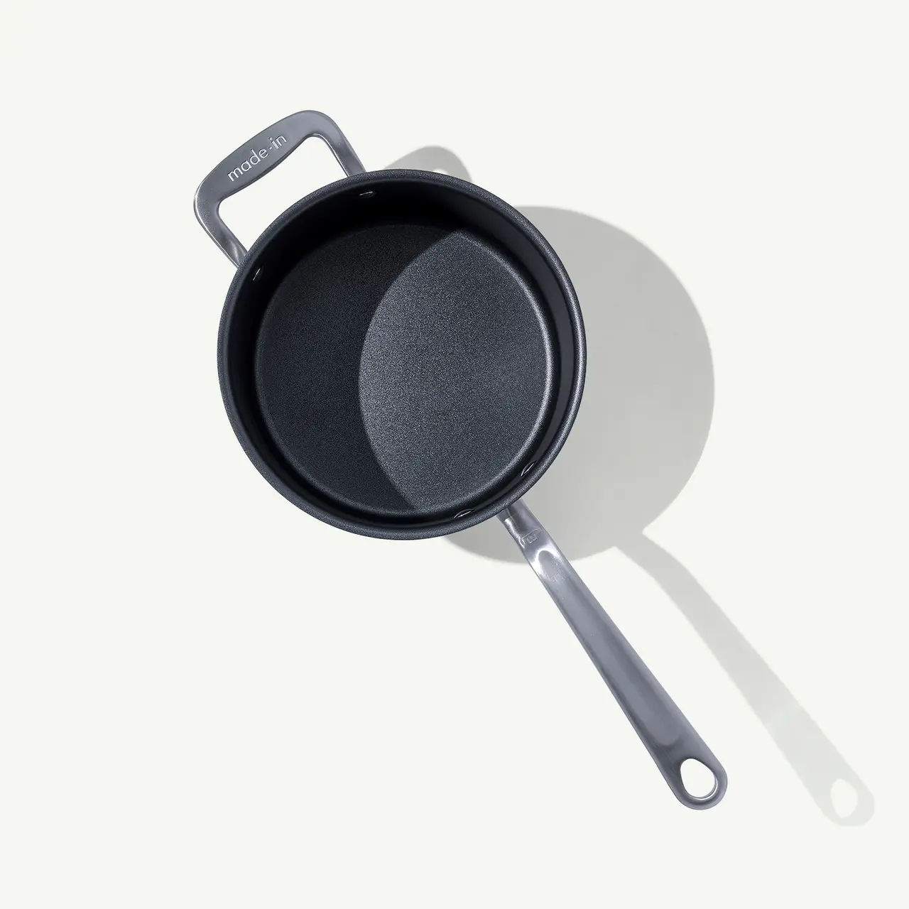 A non-stick frying pan is placed on a plain surface, casting a soft shadow.