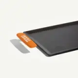 A rectangular griddle with a smooth black surface and an orange handle labeled "TEXAS" on one side.