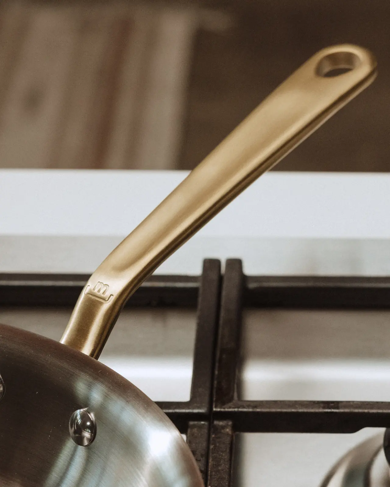 A golden-colored frying pan handle rests above a gas stove burner.