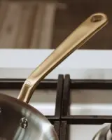 A golden-colored frying pan handle rests above a gas stove burner.
