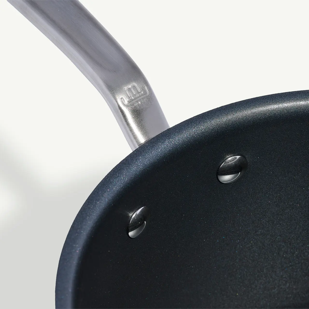 Close-up of a non-stick frying pan with a metal handle, focusing on the riveted interior connection point.