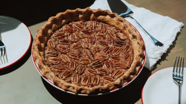 A freshly baked pecan pie sits on a table alongside plates and forks, ready to be served.