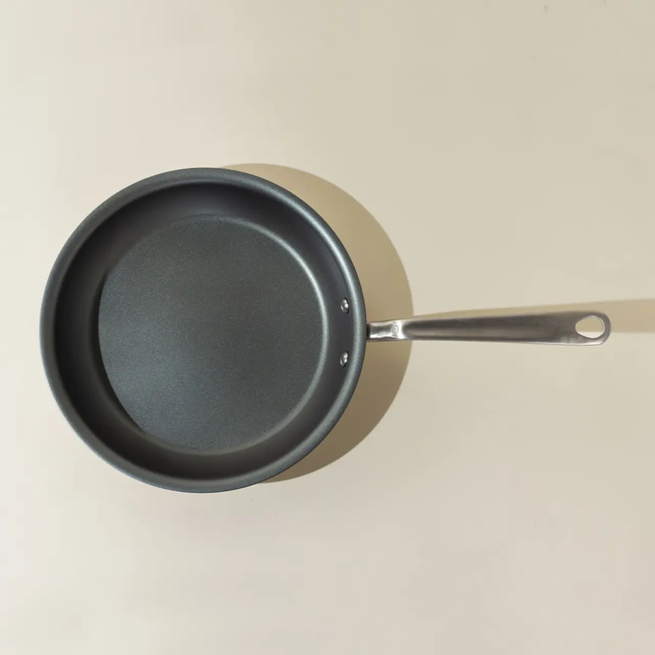 A non-stick frying pan with a stainless steel handle is positioned on a beige surface.