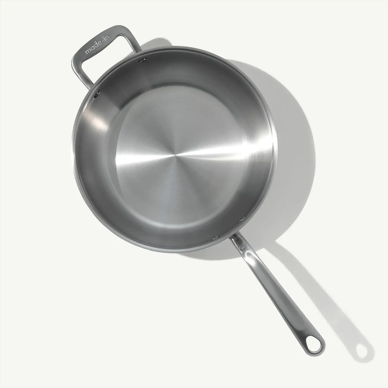 A stainless steel frying pan is shown from above casting a soft shadow on a light surface.