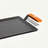 A flat, rectangular griddle with a sleek black surface and an orange handle, featuring an integrated spatula.
