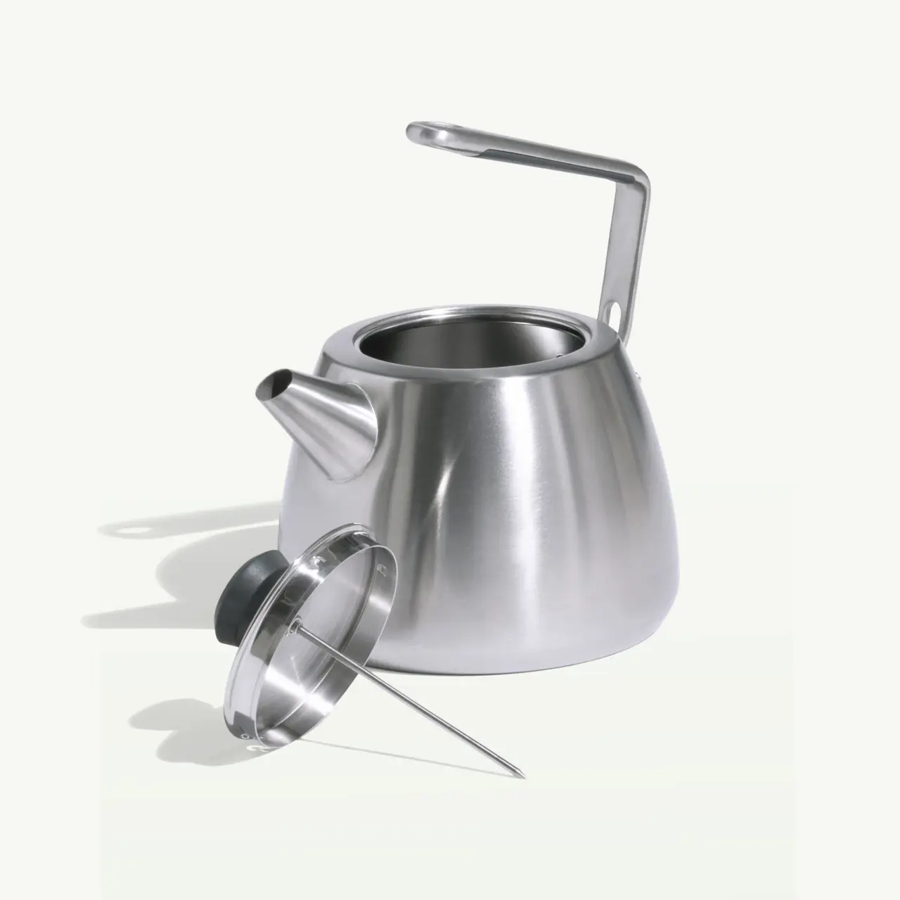 A stainless steel teapot with an attached handle and a removable lid is displayed against a light background.