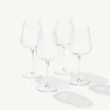 Four empty wine glasses are positioned upright on a white surface with shadows visible beneath them.