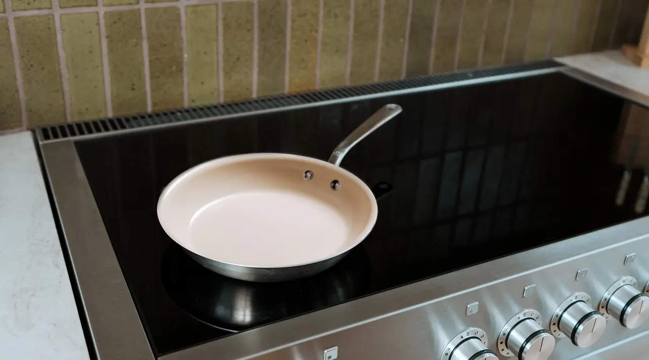 A frying pan sits on an induction stove with stainless steel control knobs and a tiled backsplash.