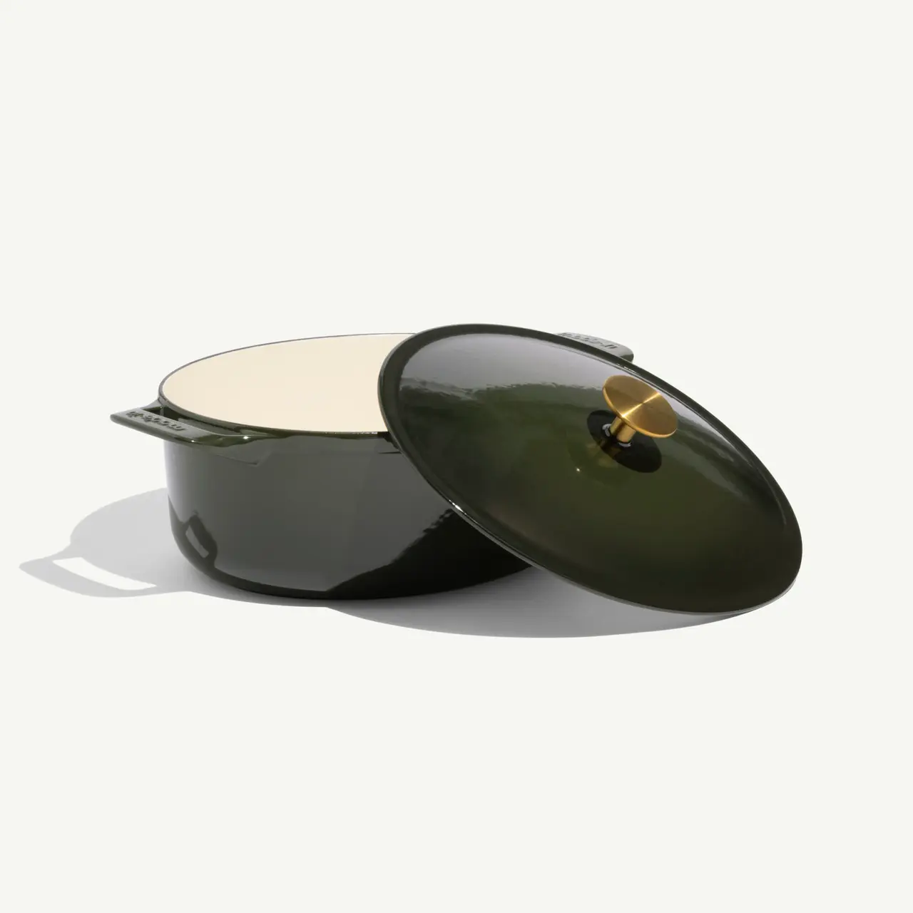 A dark green, enameled cast iron pot with a slightly ajar lid, revealing a creamy interior.