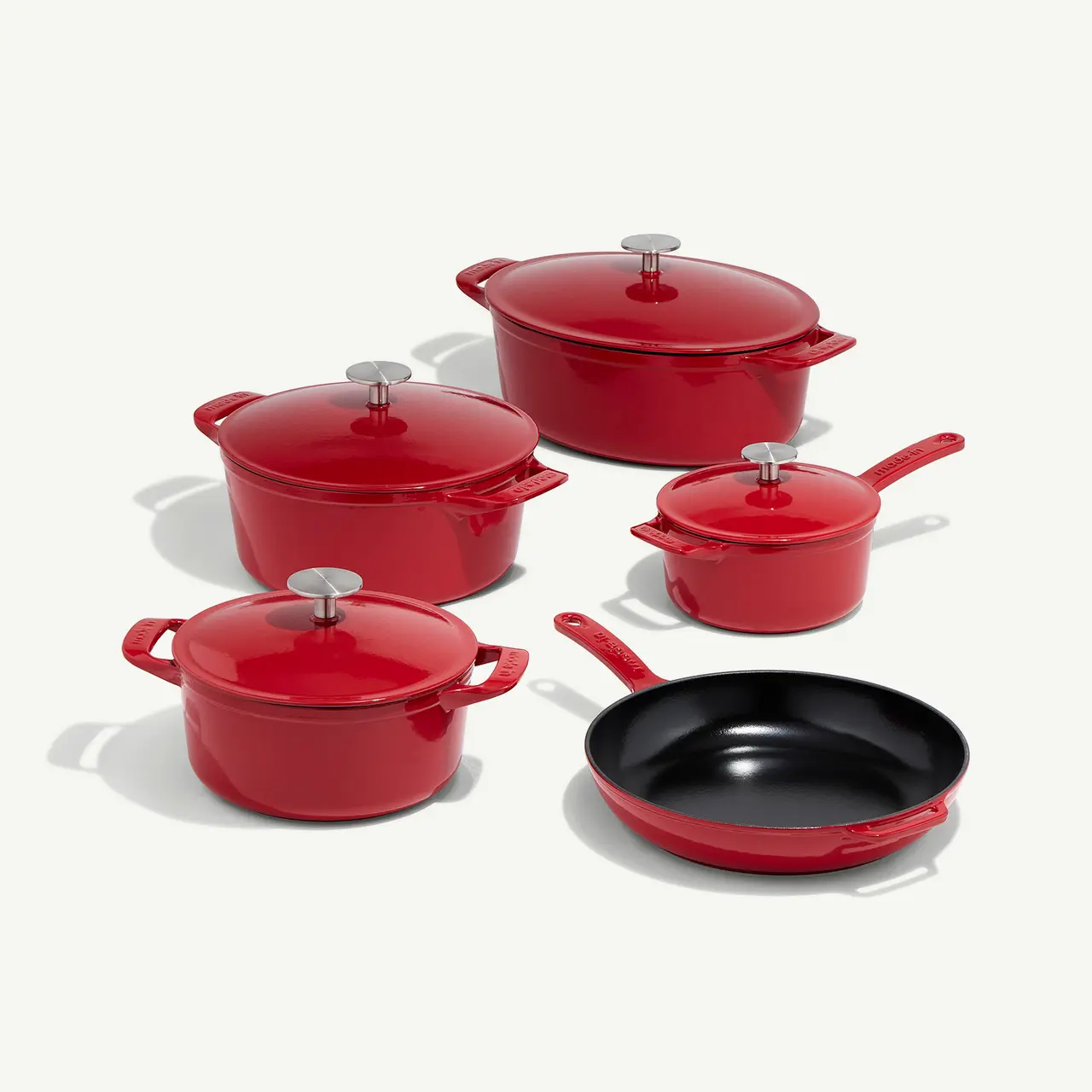 A collection of red cookware includes pots with lids and a frying pan, all with matching handles.