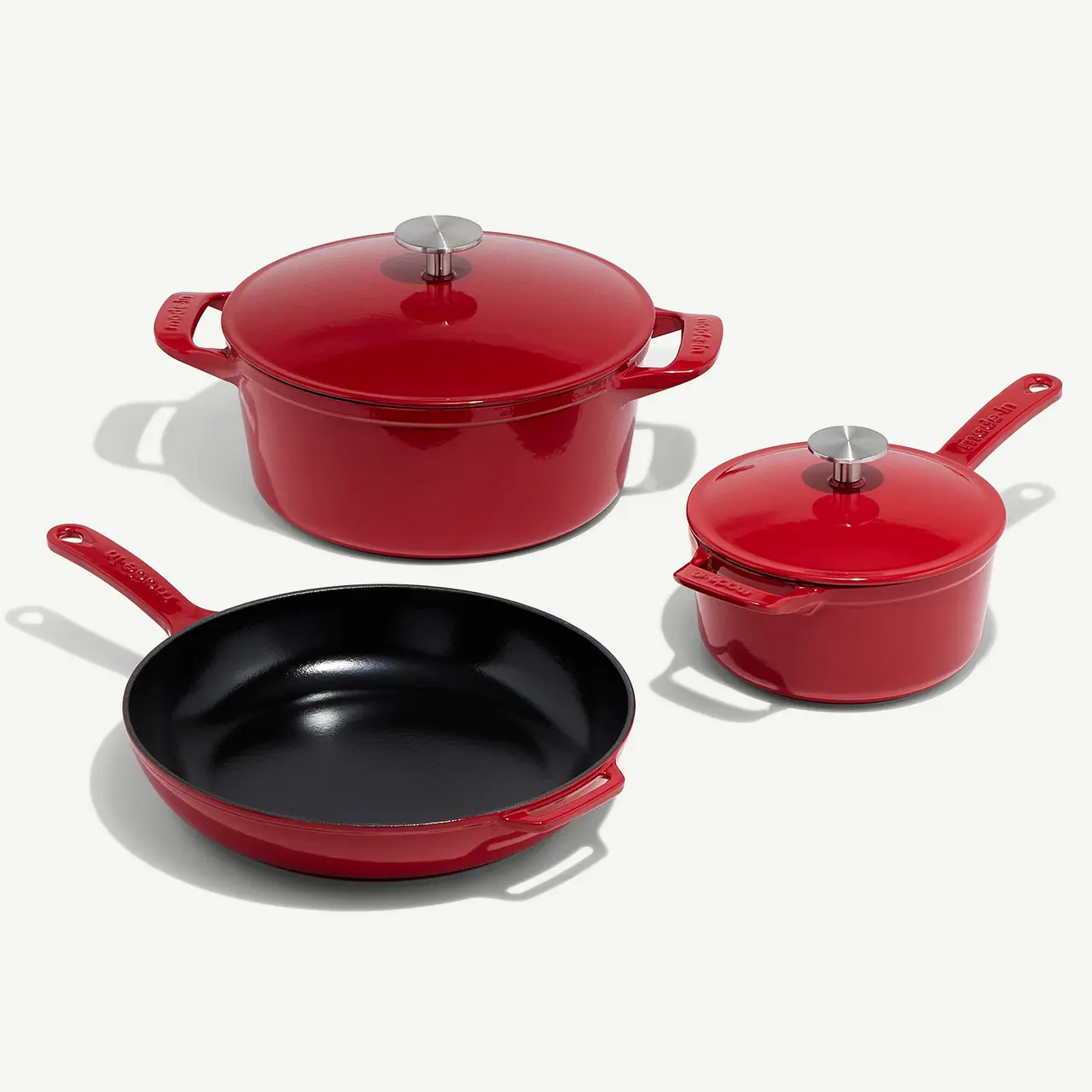 A set of red cookware consisting of a skillet, a saucepan, and a pot with lids, arranged on a light background.