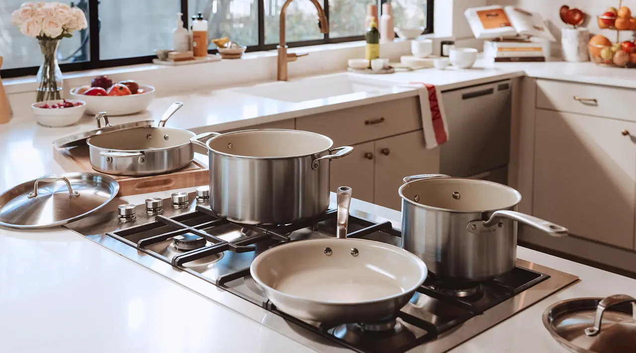 A modern kitchen features an array of stainless steel cookware on a gas stovetop, with natural light highlighting a tidy countertop and fresh ingredients nearby.