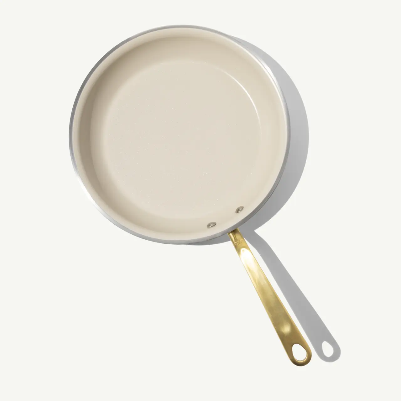 A cream-colored frying pan with a gold handle is displayed against a light background.