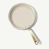 A cream-colored frying pan with a gold handle is displayed against a light background.