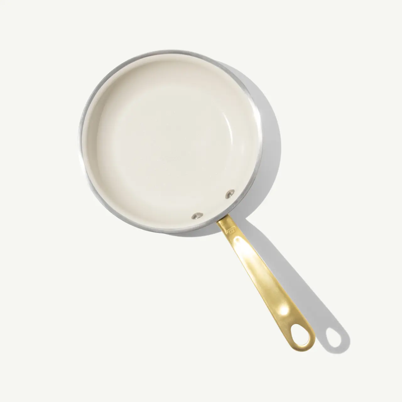 A white frying pan with a gold handle sits against a light background.