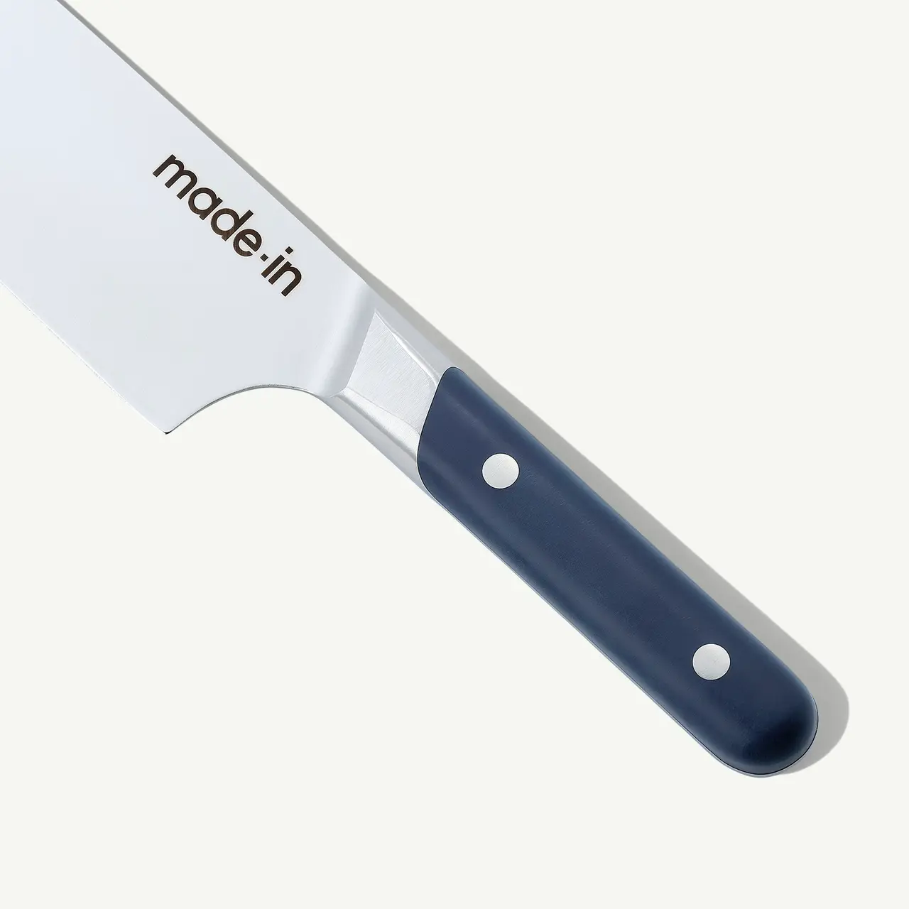A close-up of a kitchen knife with a stainless steel blade and a navy blue handle, with "made in" branded on the blade.