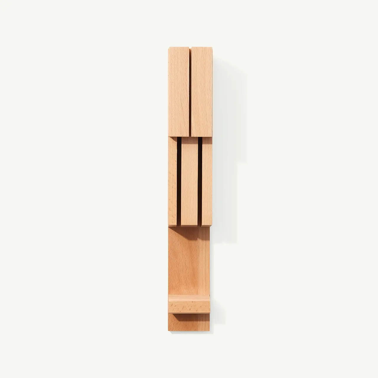 A minimalist wooden wall sconce with a vertical, linear design casts a shadow against a white background.