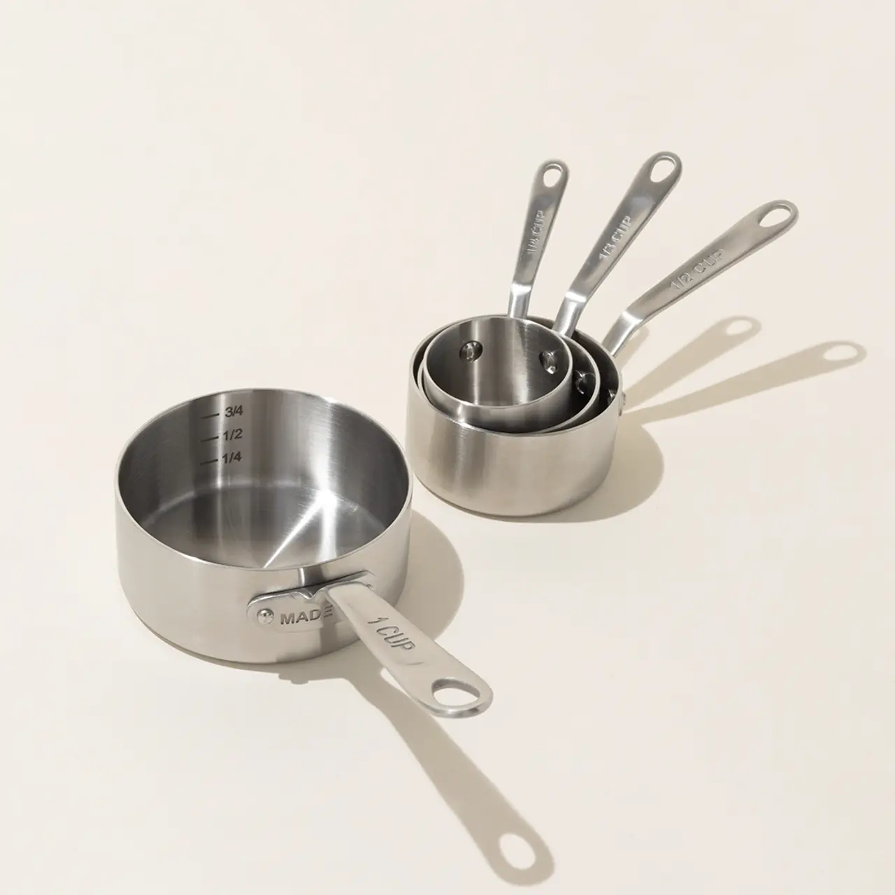 Three stainless steel measuring cups with engraved measurements sit neatly on a light surface.