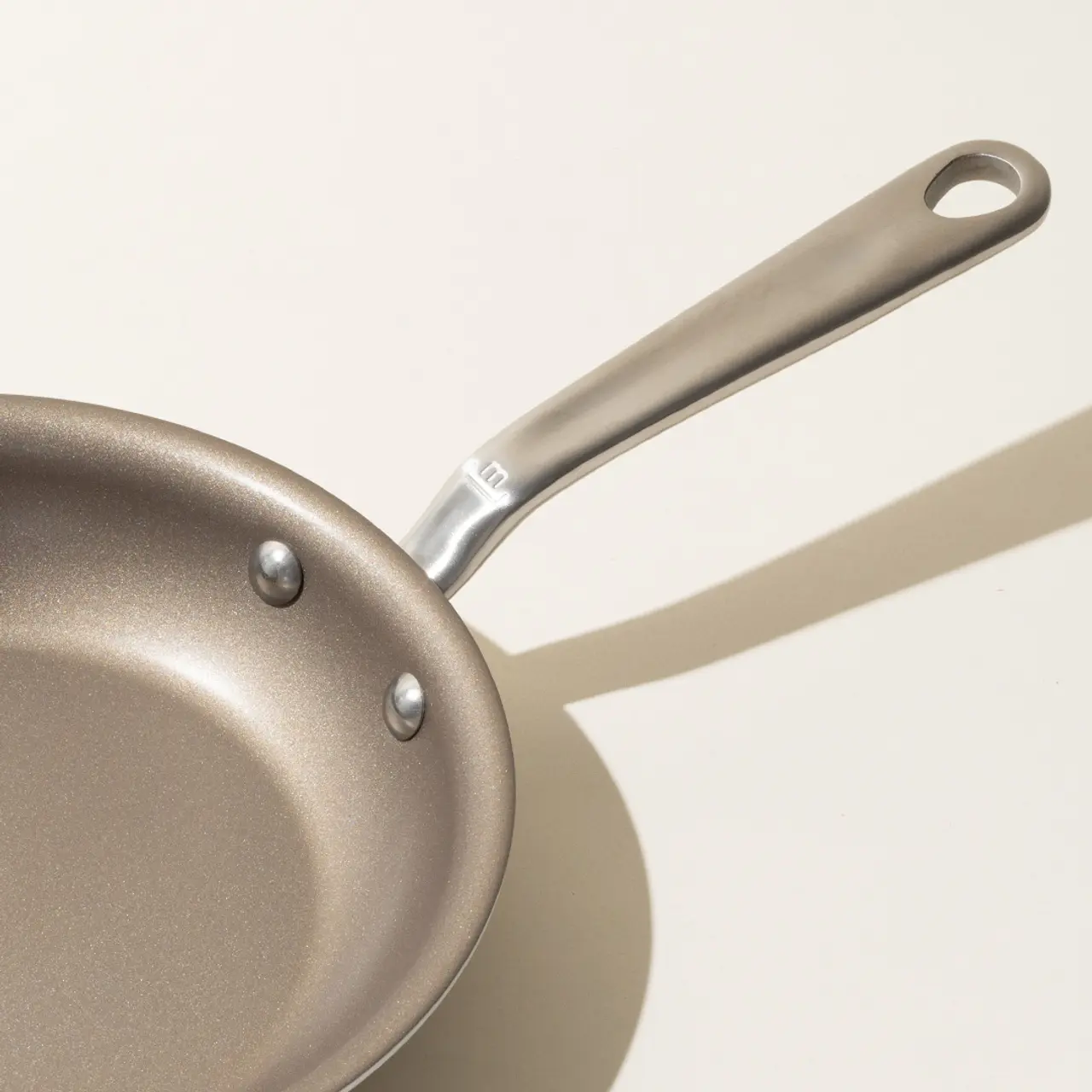 A non-stick frying pan with a stainless steel handle on a light background, casting a shadow.