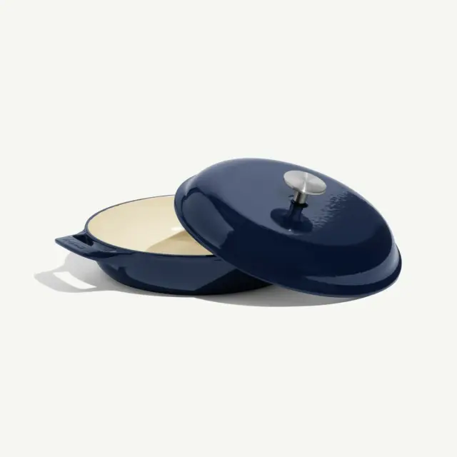 A navy-colored enameled cast iron Dutch oven with a lid is displayed partially open.