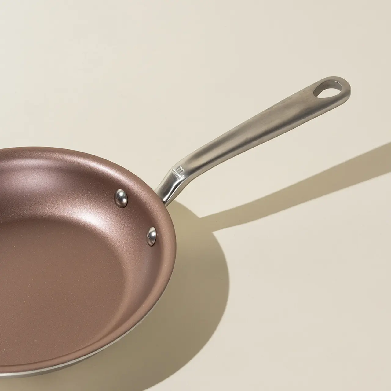 A non-stick frying pan with a stainless steel handle rests on a neutral background, casting a soft shadow.