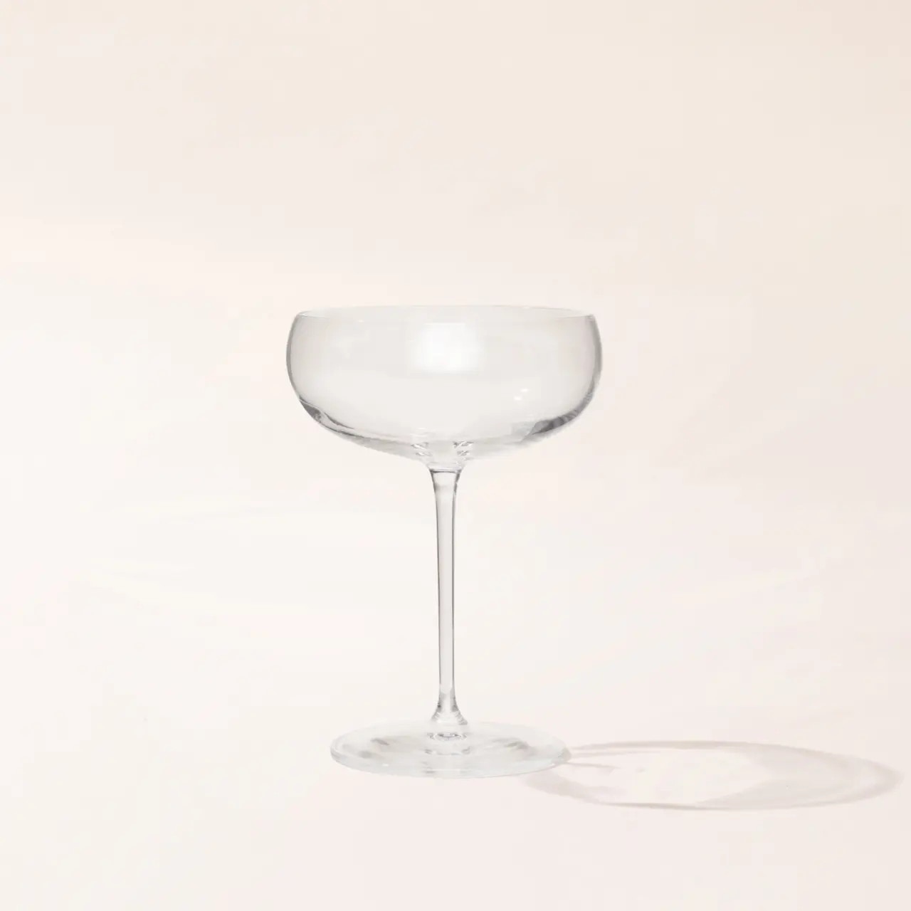 An empty glass with a stem on a cream background casting a soft shadow.