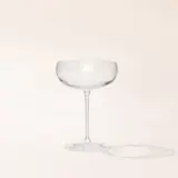 An empty glass with a stem on a cream background casting a soft shadow.