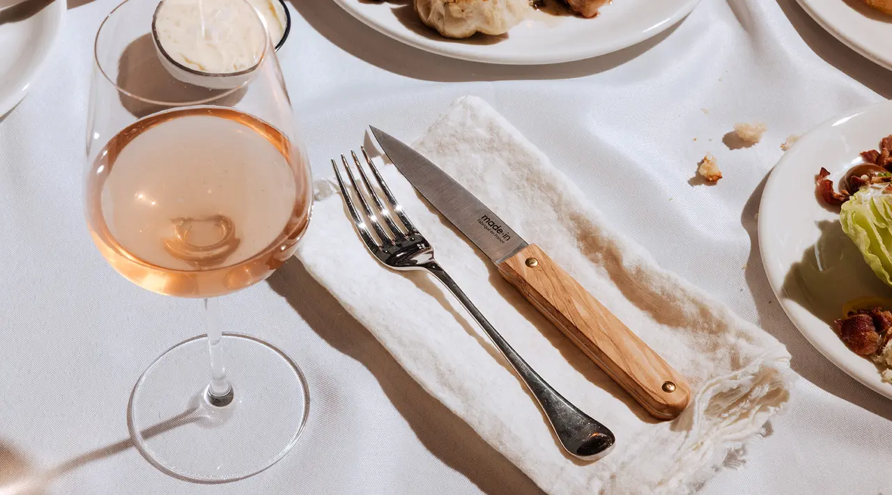 An elegant table setting with a glass of rosé wine, cutlery, and partially visible dishes suggesting a fine dining experience.