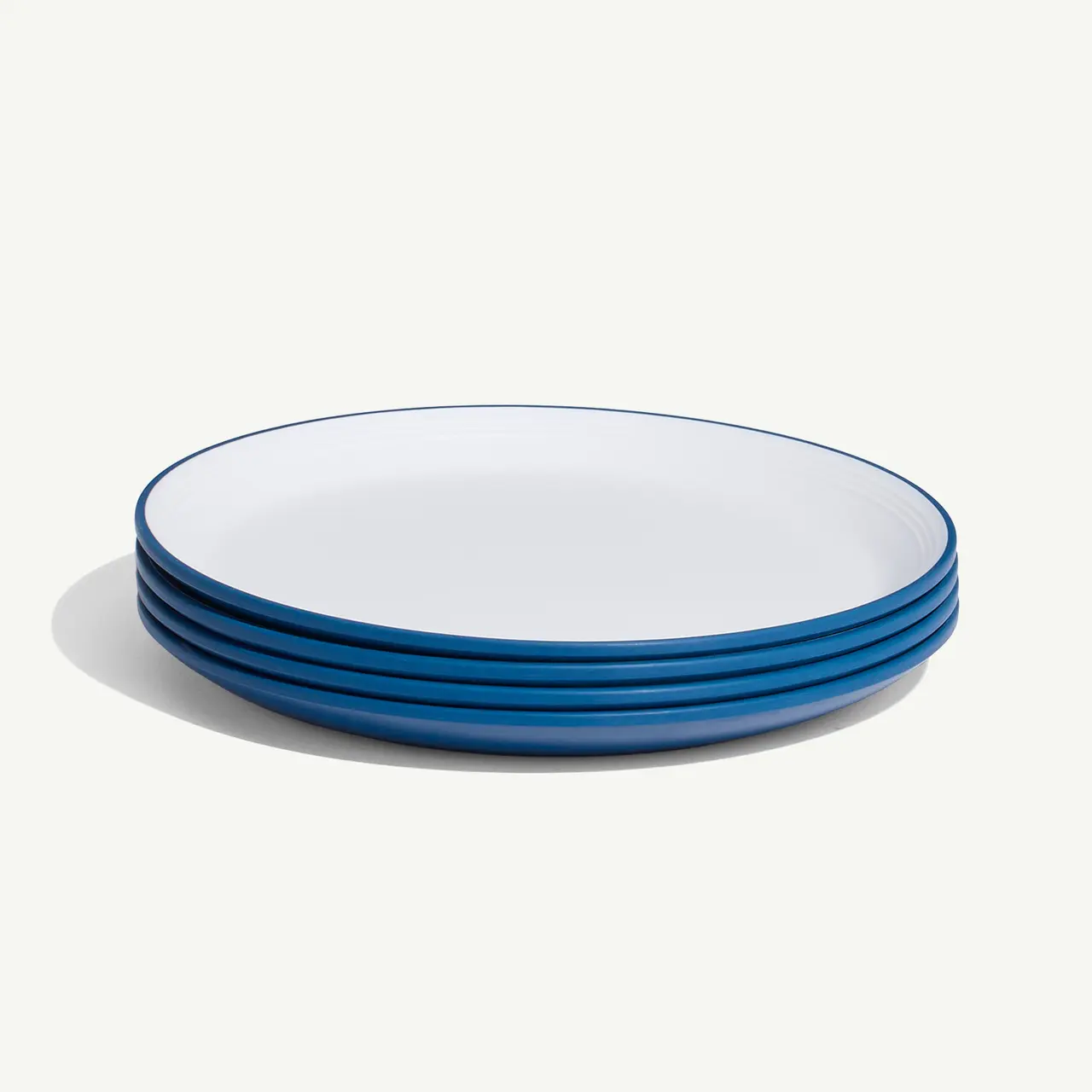 A stack of four white plates with blue rims on a white background.