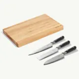 A wooden cutting board is displayed alongside three kitchen knives with black handles.