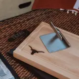 A wooden sundial with a gnomon shadow indicating the time, accompanied by a 'TEXAS' labeled bookmark, on a textured surface.